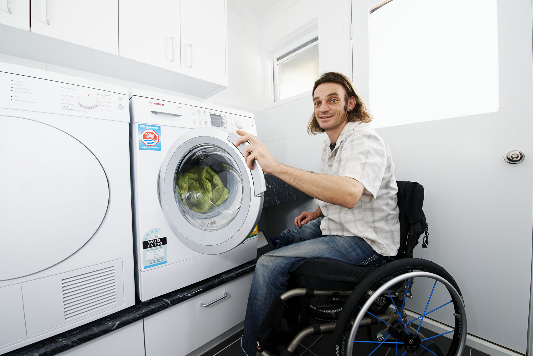 Man in wheelchair in accessible laundry loading washing machine