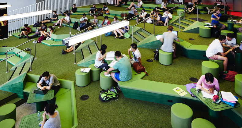 Students sitting in an open, multi-level indoor space, with benches and tables