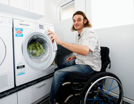 Man in wheelchair in accessible laundry loading washing machine
